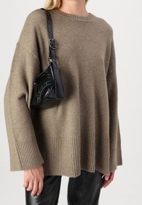 Brun stickad tröja med ribbad fåll och ärmar, kombinerad med en svart läderhandväska med runda metallaccenter.