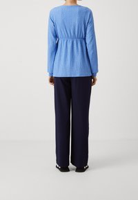 Blå texturerad långärmad topp med rynkad midja, kombinerad med marinblå vida byxor. Ovanstående outfit har enkla design detaljer och en avslappnad passform.