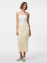 Lichte, geribbelde witte tube top gecombineerd met een middellange gestreepte gele rok; het model draagt zilveren sneakers. Glad textuur, casual ontwerp.