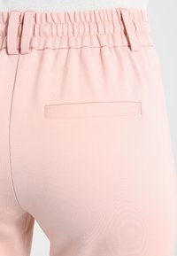 Lyserøde joggingbukser med elastisk taljebånd og en enkeltpåsyet lomme bagpå. Glat tekstur og tætsiddende design.