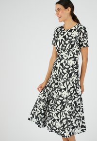 Vestido de estampado floral en blanco y negro, con mangas cortas y falda acampanada. Hecho de tela ligera con una textura suave.