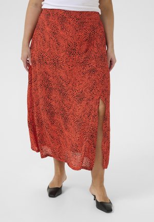 Rød midi-nederdel med sorte abstrakte pletter og en slids op til låret, båret med sorte hælede mules og en hvid top, vist fra talje til fødder.