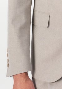 Beige suit jacket sleeve featuring a herringbone texture, a single pocket, and six cream buttons along the cuff.