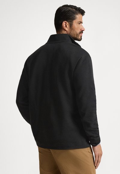 Casaco de lã polar preto com gola, mangas compridas e corte descontraído. Textura suave, detalhes mínimos, adequado para uso casual.