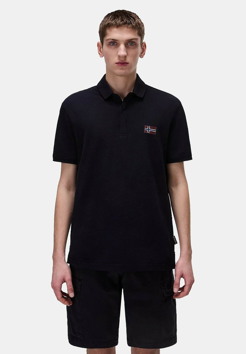 Polo shirt blu navy con design colletto e maniche corte, caratterizzato da una piccola bandiera norvegese ricamata sul petto. Indossato con pantaloni cargo neri.