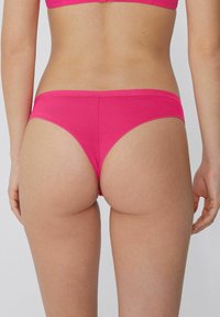 Rosa Stoff-Bikini-Unterteil mit glatter Textur, niedriger Schnitt und minimaler Bedeckung, das klare Linien und einfarbiges Design zeigt.