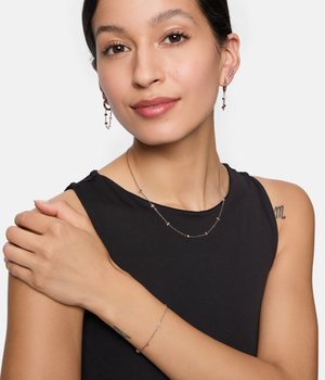 Lagdelte delikate smykker i rosaguld-tonet metal, inklusive funklende perleaccenter på en halskæde, armbånd og øreringe.