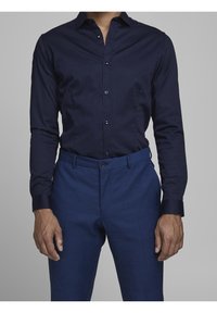 Camisa de botón de manga larga en azul marino con un corte ajustado, combinada con pantalones de vestir azules que tienen una textura suave y cierre de botón frontal.