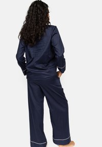 Marineblauw pyjama set met een overhemd met kraag en wijde broekspijpen. Kenmerkt zich door witte bies langs de manchetten en de zoom. Soepele stof, comfortabele pasvorm.