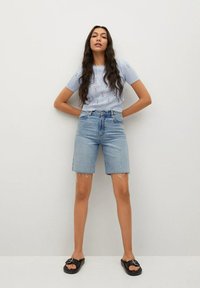 Jasnoniebieski dziergany sweter z kwiatową haftem, zestawiony z wysokim stanem szortów dżinsowych. Dopełnieniem stroju są casualowe czarne klapki.