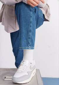 Nike Air Max 1 sportcipő fehér és világosszürke színekkel, hálós és bőr anyagokkal, valamint látható légpárnás egységgel.