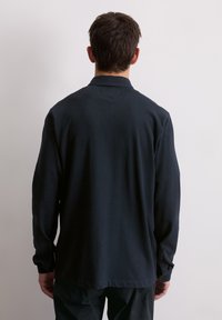 Camicia a maniche lunghe blu navy, realizzata in tessuto morbido, con colletto e polsini a bottone. Il retro presenta un orlo dritto e dettagli minimi.