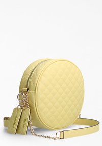 Okrągła żółta pikowana torba ze sztucznej skóry z zamknięciem na zamek błyskawiczny oraz odpinanym łańcuszkowym paskiem, ozdobiona metalowymi detalami.