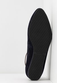 Ballerine en daim bleu marine avec une semelle en caoutchouc noir texturée. Présente un bout rond et un design minimaliste avec une découpe sur le côté.