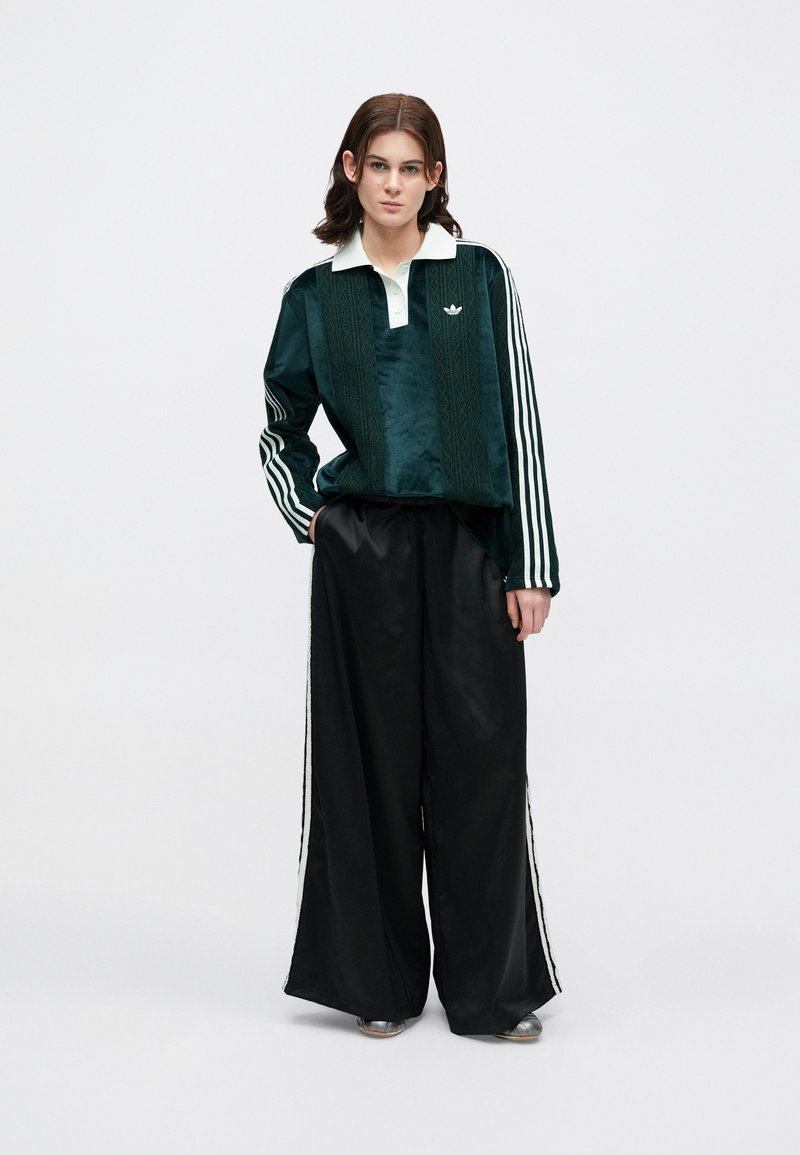 Green velour jacket with a white collar, featuring tonal embroidery and three white stripes on sleeves. Black satin wide-leg pants with side stripes.