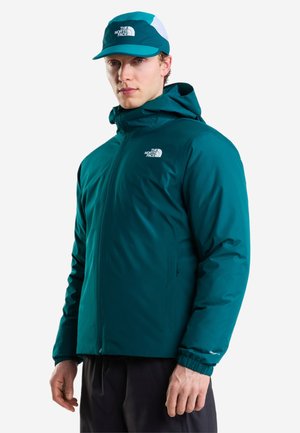 Homme portant une veste à capuche bleu sarcelle et une casquette assortie de la même couleur avec le logo The North Face sur les deux vêtements, debout sur fond blanc.