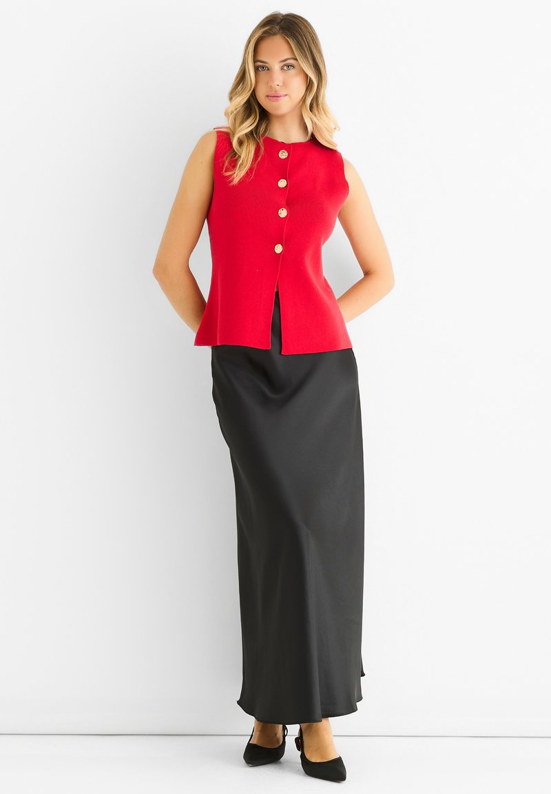 Red sleeveless top with gold button detailing, paired with a black long skirt. The top has a flared design and a round neckline.
