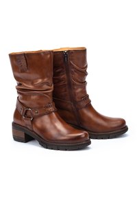 Bottes ankle en cuir marron avec un design légèrement affaissé, fermeture éclair latérale et détail de sangle tressée. Talon épais et semelle texturée.