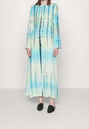 Langærmet kjole i mellem længde med en gradient mønster i blå og grøn batik og sorte detaljer. Båret med teksturerede sorte slip-on sko.