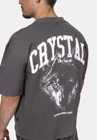 Šedá oversized košile s grafickým motivem bílého vlka a nápisem "CRYSTAL Paříž" na zadní straně. Měkká tkanina s uvolněným střihem.