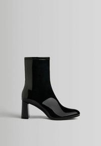 Czarne botki sięgające do kostki, z eleganckim wykończeniem z lakierowanej skóry, kwadratowym obcasem, spiczastym noskiem oraz kontrastującą matową teksturą na cholewce.