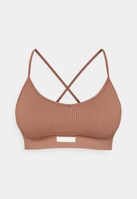 Rebrasta smeđa bralette s tankim, ukrštenim trakama i bijelom etiketom na dnu. Mekani materijal, bezšavna izrada i rastezljiv materijal.