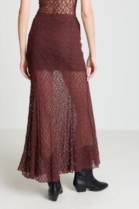 Bordeauxfarbener Spitzenrock mit transparenter Textur, mit langem, fließendem Design, das bis zu den Knöcheln reicht, kombiniert mit schwarzen, spitz zulaufenden Stiefeletten.