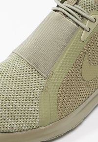 Zelená sportovní obuv s texturovaným síťovaným svrškem, elastickým popruhem a hladkými akcenty. Obsahuje zaoblenou špičku a flexibilní podrážku.