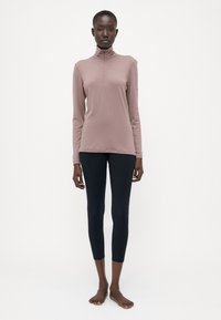 Hosszú ujjú, világos rózsaszín póló, magas nyakkal és cipzárral; fekete, testhezálló leggings-szel párosítva, amely sima textúrával rendelkezik.