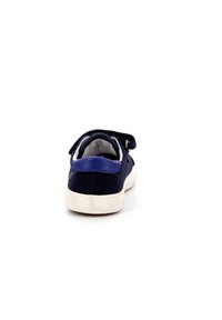 Zapato de ante azul marino con suela blanca, que presenta una correa de velcro y un panel posterior texturizado. Diseño simple con detalles mínimos.