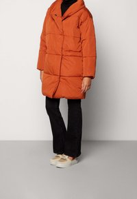 Puffjacka i bränd orange, med en stor krage, quiltat mönster och framknäppning. Matchad med svarta byxor och lätta sneakers.