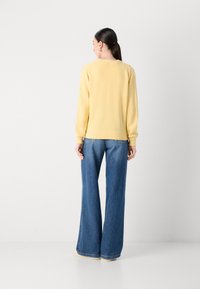 Žlutý pletený svetr s rytím na manžetách, spárovaný s volnými modrými džíny. Svetr má kulatý výstřih a uvolněný střih.