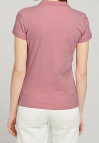 Rosa kurzärmeliges Poloshirt mit geripptem Kragen, glattem Stoff und figurbetontem Schnitt, von hinten vor neutralem Hintergrund gesehen.