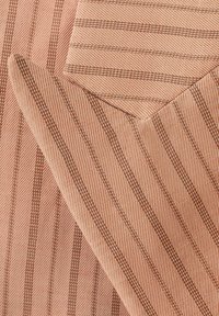 Gros plan sur un tissu beige avec de fines rayures verticales marron et un coin plié montrant un motif à rayures diagonales.