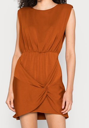 Rostbruine jurk met mouwloos ontwerp, geplooide taille en gedraaide knoopdetail aan de zoom, gemaakt van zachte, lichtgewicht stof.