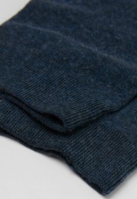 Marineblaue Strickschal, hergestellt aus weichem Stoff, zeichnet sich durch eine gerippte Textur und eine gefaltete Kante aus, die feine Details und gleichmäßige Nähte zeigt.