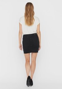 Falda corta de mezclilla negra con un diseño de bolsillo trasero, que cuenta con un lazo para cinturón y un corte recto. Combinada con una camiseta de color claro.