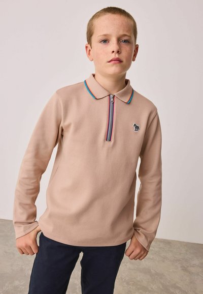 Helle beige Polohemd mit Reißverschluss und einem bunten gestreiften Kragen sowie einem kleinen gestickten Logo auf der Brust, kombiniert mit dunkelblauen Hosen.