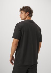 Svart bomullst-shirt med korta ärmar, rund halsringning och avslappnad passform, sedd bakifrån. Slät textur, minimalistisk design.