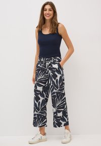 Navy tanktop gecombineerd met wijde broek met een witte achtergrond en grote marineblauwe bladvormen. De broek heeft zakken en een koordsluiting.