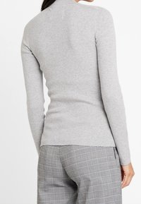 Szary, prążkowany sweter typu golf z długimi rękawami, o dopasowanym kroju i lekko zaokrąglonym dolnym brzegiem. Noszony z spodniami w kratę.