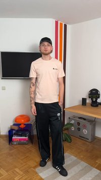 Ανοιχτό ροζ μπλουζάκι με μαύρο κείμενο, σε συνδυασμό με μαύρο παντελόνι φόρμας που έχει λευκές ρίγες στο πλάι. Ένα μαύρο καπέλο και σκούρα υποδήματα ολοκληρώνουν την εμφάνιση.