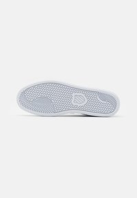 Valkoinen tennarin pohja, jossa on teksturoidun kuvion, sisältäen herringbone-mallin ja keskitetyn logoaksentin. Sileää kumimateriaalia.