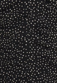 Černá látka s bílými nepravidelnými puntíky a skládáním, nařasenou texturou podél centrálního švu.