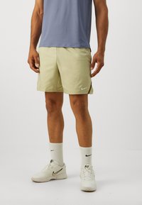 Nike herre sportshorts i lys gul med et geometrisk mønster, der har et logo, og parret med hvide sokker og sko.