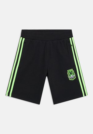 Short de sport noir avec des bandes latérales vert vif et un patch personnage pixélisé vert près de la poche droite.