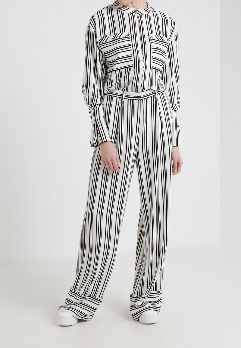 Svartvitrandig blus med två framfickor, knappstängning, och bälte, högmidjade randiga byxor med avslappnad passform och vida ben.