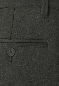 Pantalones grises con un bolsillo trasero que tiene un botón negro. La tela presenta una textura sutil, lo que realza su aspecto moderno.