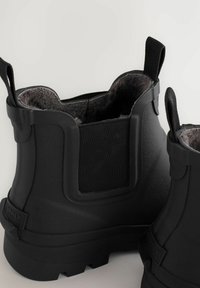 Schwarze Gummistiefeletten mit elastischen Seitenteilen, strukturierter matter Oberfläche und weichem grauem Innenfutter. Mit Zuglaschen für einfaches An- und Ausziehen.