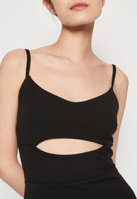 Černé bezramenné šaty s výstřihem do V a výřezem v oblasti pasu, vyrobené z hladkého materiálu, který zdůrazňuje těsně přiléhající siluetu.